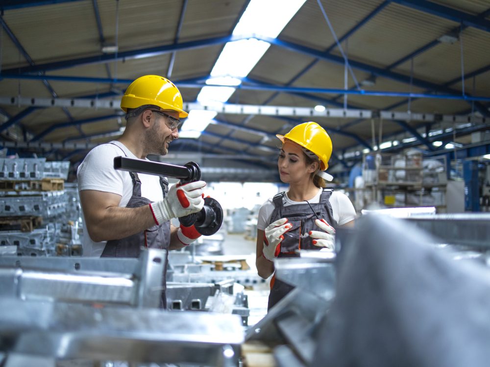 Workers checking quality of metal parts manufactured in factory.